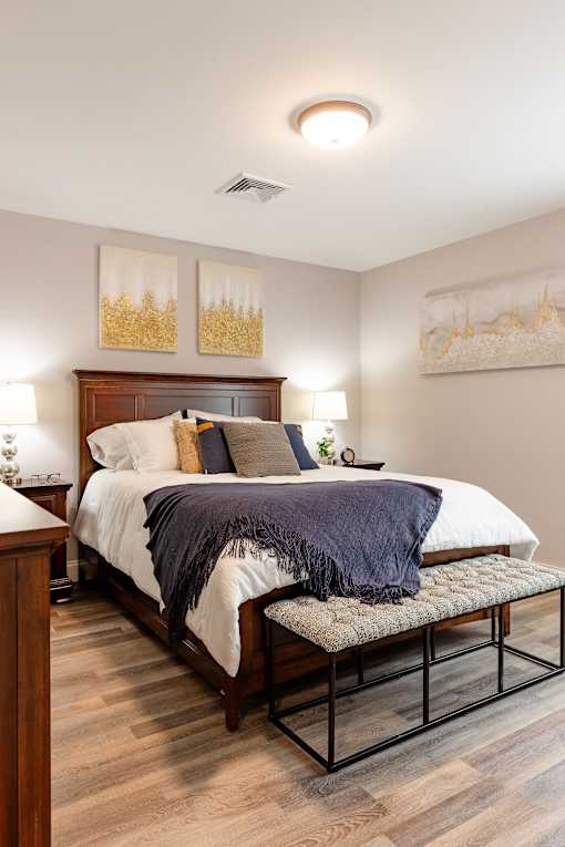 A bedroom with a bed, nightstand, and two wall art pieces.