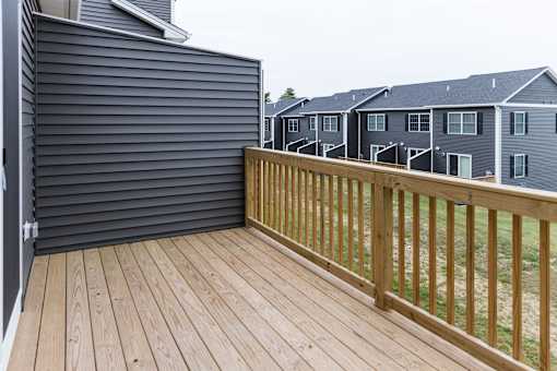 A wooden deck with a railing and a grey house in the background.