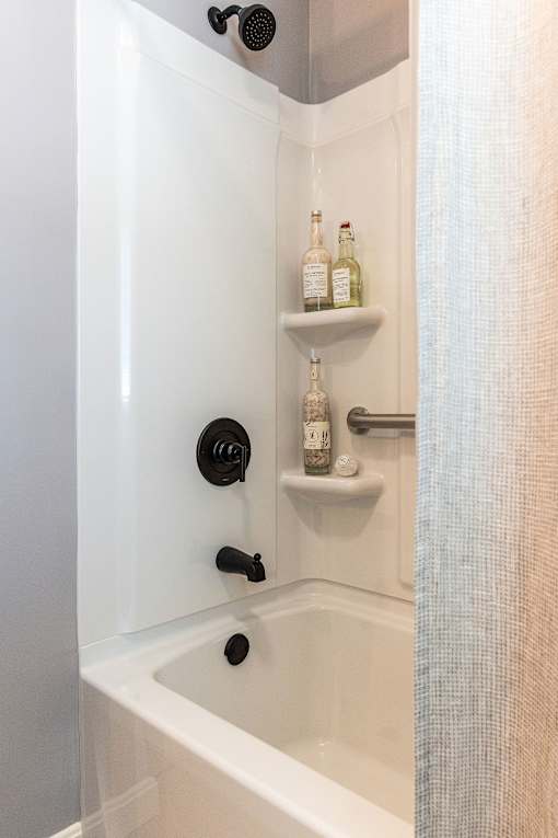 A white bathtub with a shower head and a shelf with bottles on it.