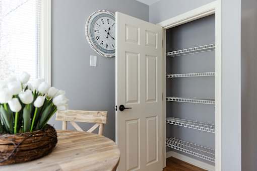 A white door is open to a hallway with shelves.