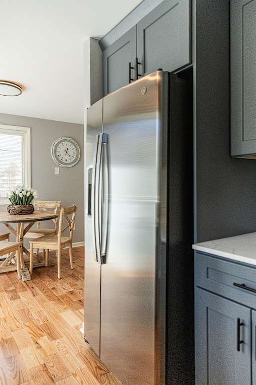 A stainless steel refrigerator stands in a kitchen with wooden flooring.