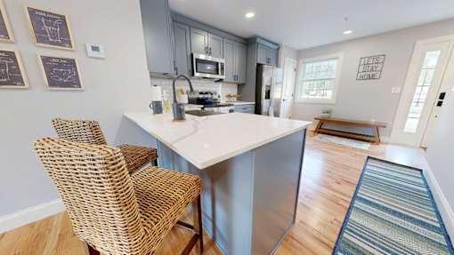 A kitchen with a white island and two wicker chairs.