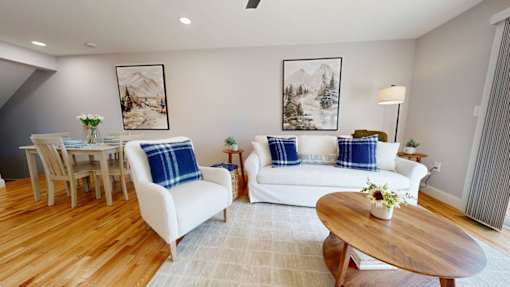 A living room with a white couch, a wooden coffee table, and a dining table with chairs.