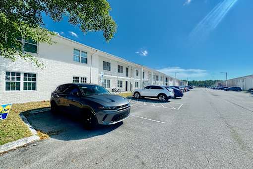 A black car is parked in a parking lot in front of a white building.