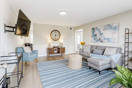 A living room with a grey couch, a blue chair, and a clock on the wall.