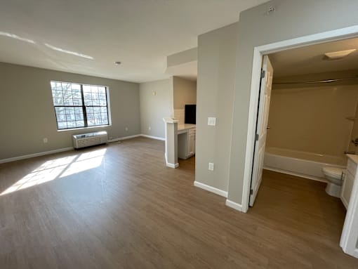 A large, empty room with a window and a door leading to another room.