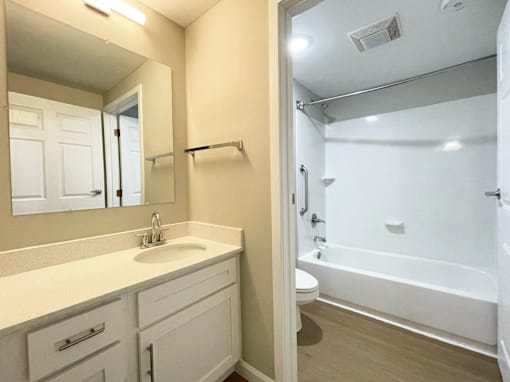 A white bathroom with a sink, mirror, and bathtub.