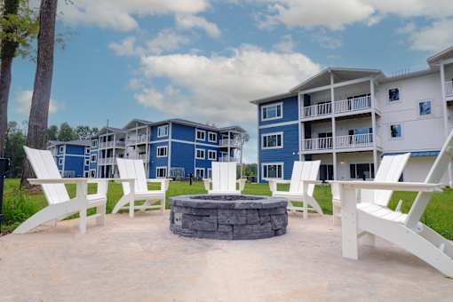 our fire pit is in front of our blue apartments with white chairs and benches