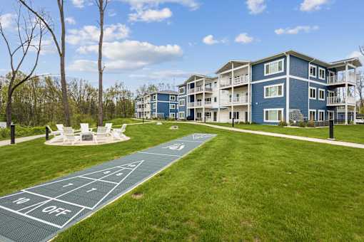 A blue and white apartment building with a green lawn and a shuffleboard court.