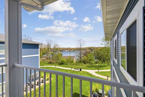 A balcony overlooks a green lawn and a body of water.