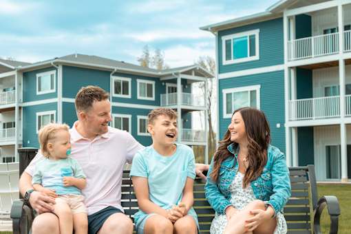 A family of four is sitting on a bench outside a blue building.
