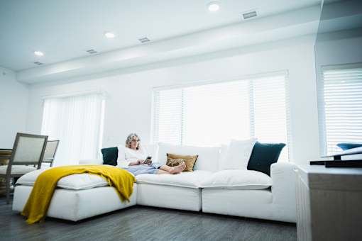 A woman is sitting on a white couch with a yellow blanket.