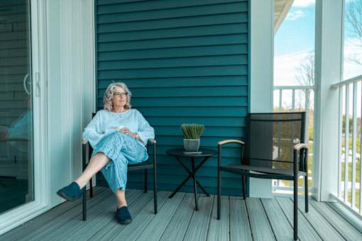 A woman in blue pajamas sits on a porch.