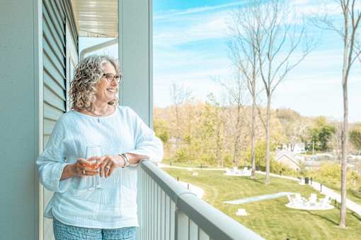 A woman with glasses is standing on a balcony holding a glass.