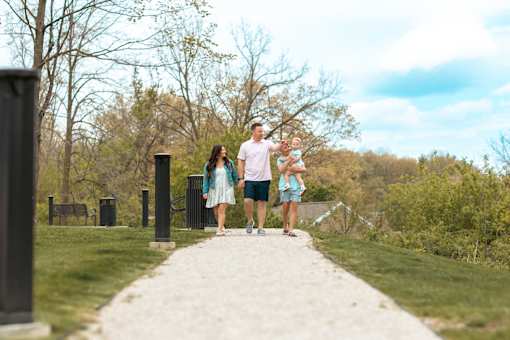 A family of three is standing on a gravel path in a park.