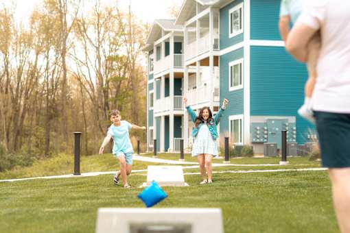 A woman and a child are playing with a blue ball in front of a blue and white building.