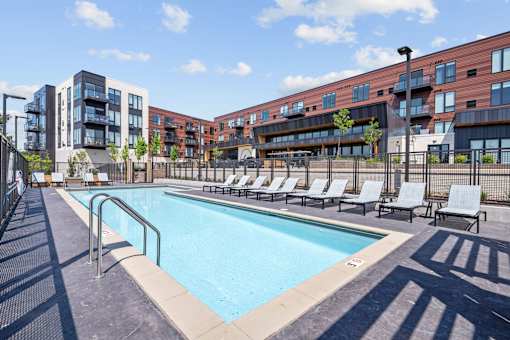 A swimming pool surrounded by lounge chairs and apartment buildings.