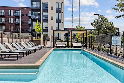 A large swimming pool in front of a building with lounge chairs around it.
