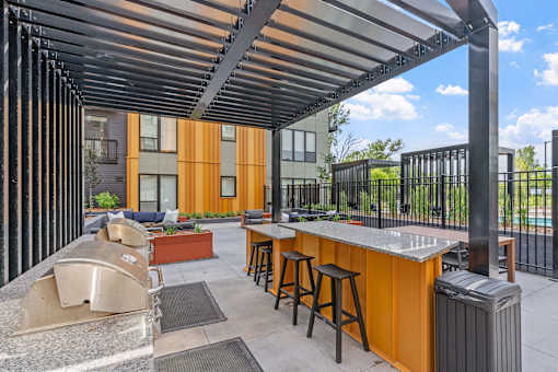 A patio with a bar and stools under a roof.