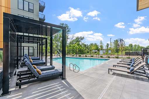 A pool area with sun loungers and a building in the background.