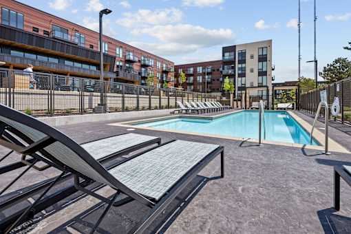 A pool area with sun loungers and a fence in front of apartment buildings.