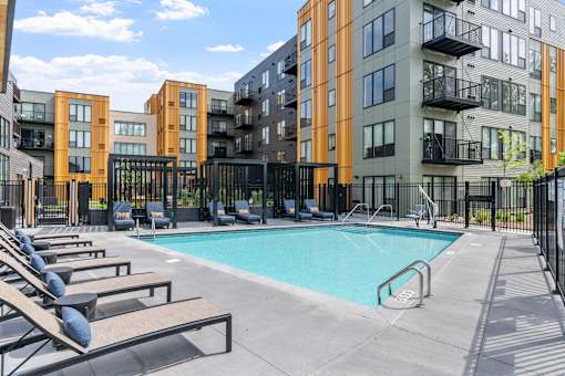 A swimming pool surrounded by lounge chairs and apartment buildings.