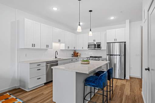 A kitchen with white cabinets and a white island with blue chairs.