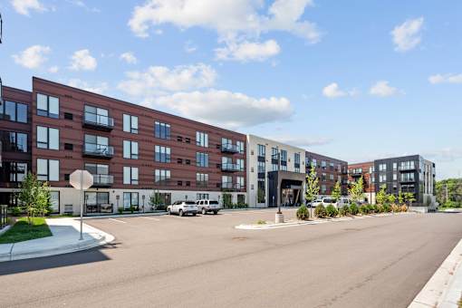 A street view of a residential area with apartment buildings and cars parked on the side of the road.