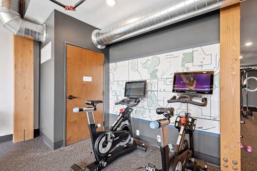 A room with a bike workout station and a TV screen showing a woman exercising.