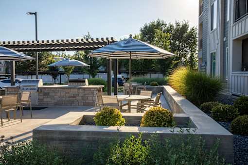 A patio with a table and chairs under umbrellas at Parc on 5th Apartments & Townhomes