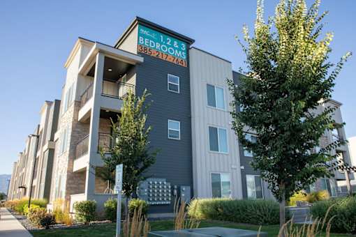 A modern apartment building with a sign that reads "1, 2 & 3 Bedroom" and a phone number.