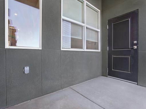 A grey wall with a black door and a window.