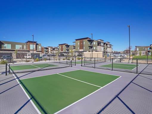 A tennis court is surrounded by apartment buildings.