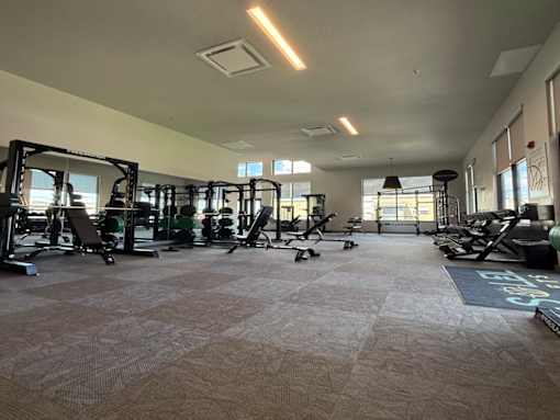 A spacious gym with various exercise equipment and a grey carpeted floor.