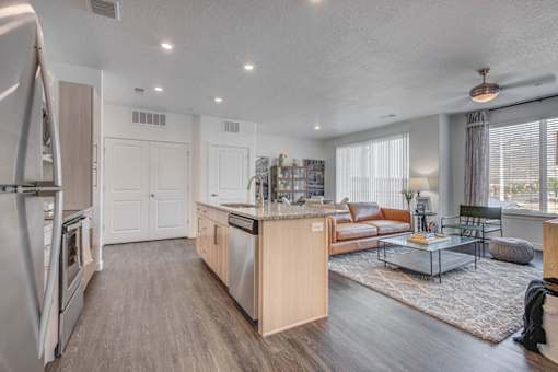 A modern kitchen with a refrigerator on the left and a dining area with a glass table and chairs.