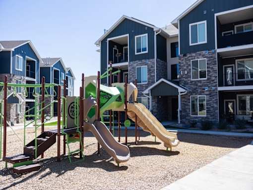 A playground with a green and tan slide in front of a building.