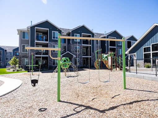 A playground with swings and a slide in front of apartment buildings.