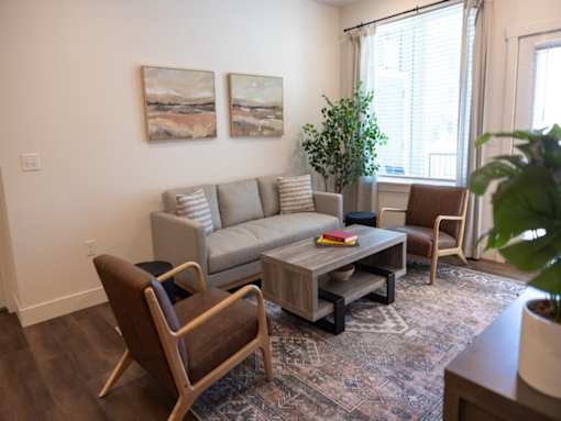 A living room with a grey couch, a brown chair, a coffee table, and two paintings on the wall.