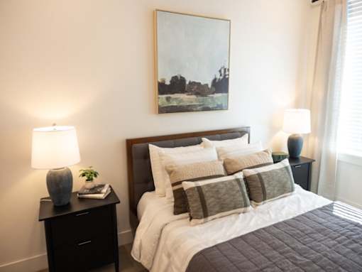 A bedroom with a bed, nightstand, and a painting on the wall.