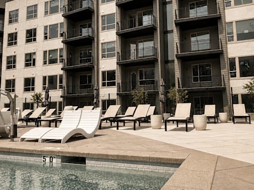 A pool area with sun loungers and apartment buildings in the background.