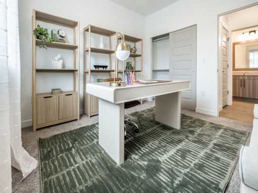 A white desk with a lamp and a green rug in front of it.