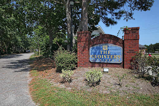 The entrance to The Cloisters with a blue sign on a brick wall. The Cloisters Apartments, 902 67th Avenue North, Myrtle Beach, SC