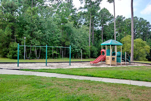 A playground with a green swing set and a red slide. Aviary Village Apartments, in Conway, SC 29526