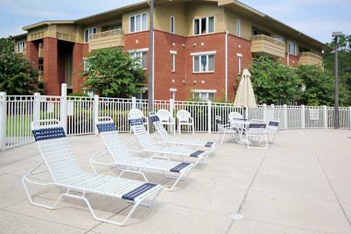 Aviary Village Apartments, in Conway, SC 29526 A white and blue lounge chair is in front of a red brick building.