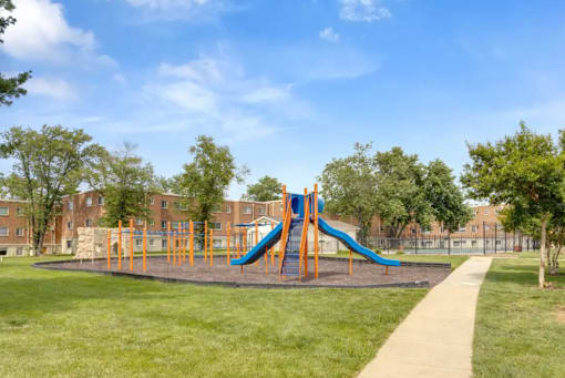 A playground with a blue and orange slide in the middle of a grassy area at Resident Parking at The District at Forestville Apartments, Forestville, MD, 20747