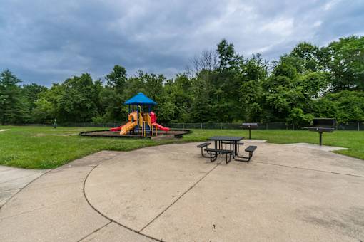 A playground with a blue and yellow slide, picnic tables, and a concrete area.
