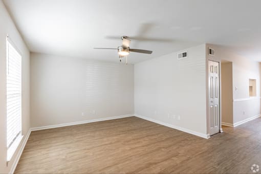 A room with a ceiling fan and light fixture, wooden flooring, and white walls.