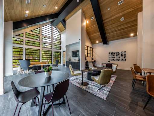 A clubhouse with four seating areas and a lounge near large floor to ceiling windows and a vaulted ceiling.