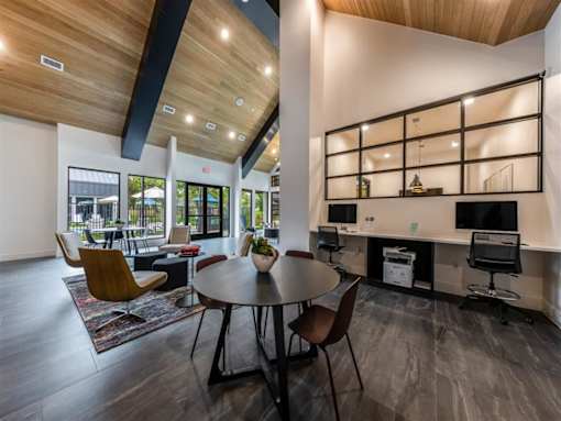 A clubhouse with four seating areas and a built-in office area with two chairs, a printer, and two computers near doors leading to a community pool.