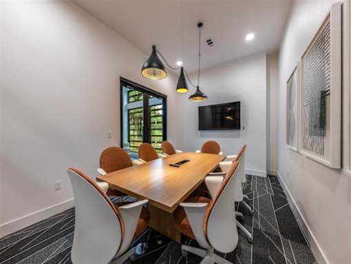 A resident conference room with a long wooden table, 4 modern chairs, a TV, and pendant lights.